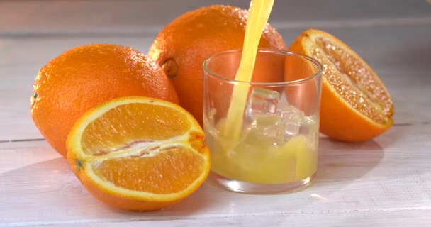 Primer plano. El jugo de naranja se vierte en un vaso. hay naranjas frescas en la mesa cercana — Vídeos de Stock