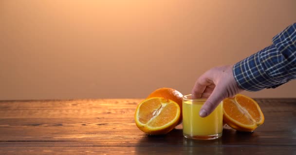 Mans kézzel vesz egy friss narancslevet az asztalról. A narancs a fekete fa asztalon van. — Stock videók