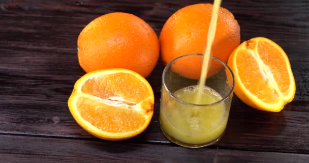 Close-up. suco de laranja é derramado em um copo. há laranjas frescas na mesa nas proximidades — Vídeo de Stock