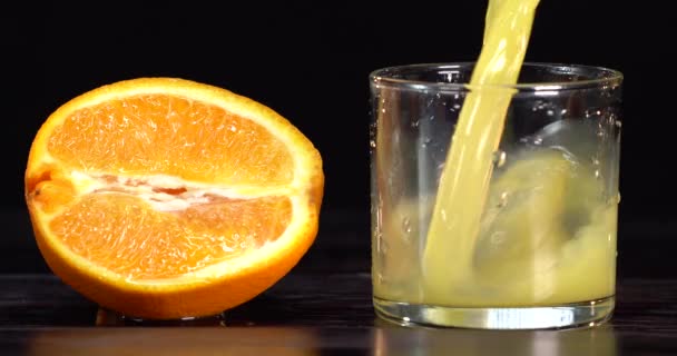Apelsinjuice hälls i ett glas. det finns färska apelsiner på bordet i närheten. Mörkt bord — Stockvideo