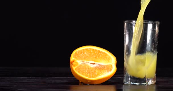 El jugo de naranja se vierte en un vaso. hay naranjas frescas en la mesa cercana. Mesa oscura — Vídeos de Stock