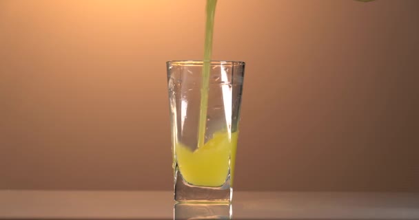 Χύνεται χυμός πορτοκαλιού σε ένα ποτήρι. Φόντο ηλιοβασιλέματος — Αρχείο Βίντεο