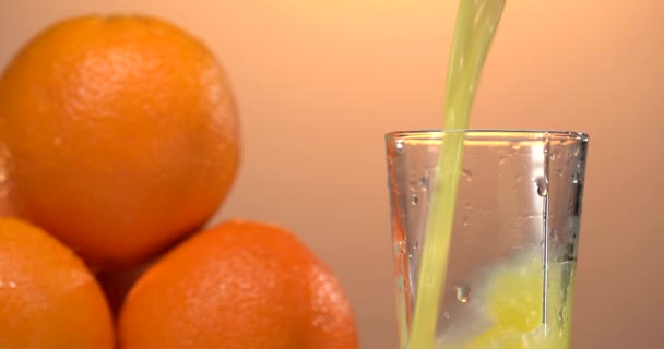 El jugo de naranja se vierte en un vaso. hay naranjas frescas en la mesa cercana. fondo del atardecer — Vídeos de Stock