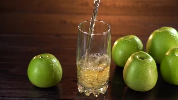 Свежий яблочный сок наливают в стакан на стол из темного дерева в замедленной съемке — стоковое видео