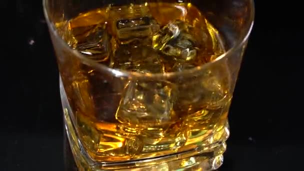 Verter Whiskey en el vidrio con cubitos de hielo a 100fps con movimiento de cámara. A cámara lenta. El barman arroja hielo al alcohol. Fondo oscuro — Vídeos de Stock