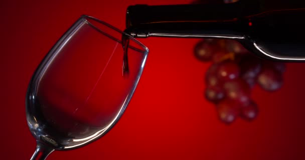 Le vin rouge est versé dans un verre à partir d'une bouteille sur un fond rouge. Détail du mouvement super lent prise de vue de verser du vin rouge de bouteille sur fond de dégradé rouge de luxe — Video