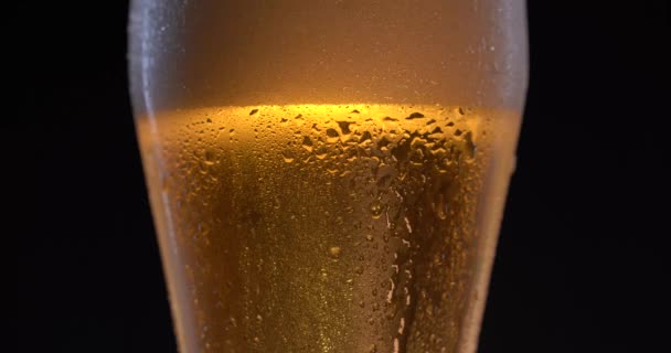 Studené řemeslné pivo s kapkami na skle, bublinami a pěnou stoupají. Sklenici piva. Alkohol. Černé pozadí — Stock video
