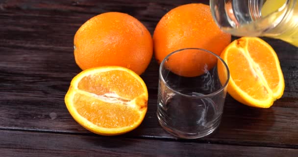 特写。橙汁倒入杯子里。附近的桌子上有新鲜的橙子 — 图库视频影像