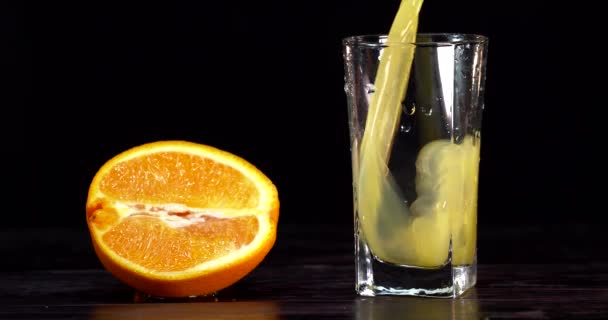 Närbild. Apelsinjuice hälls i ett glas. det finns färska apelsiner på bordet i närheten — Stockvideo