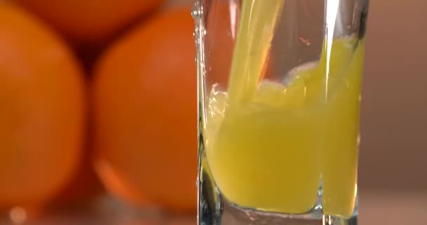 Apelsinjuice hälls i ett glas. det finns färska apelsiner på bordet i närheten. solnedgång bakgrund — Stockvideo