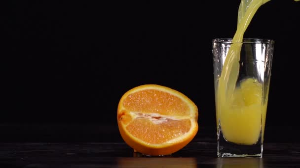 Despeje o suco de laranja em um frasco de vidro em um fundo branco e tenha a garrafa de suco de laranja pronta. Laranja cortada ao meio como fundo — Vídeo de Stock