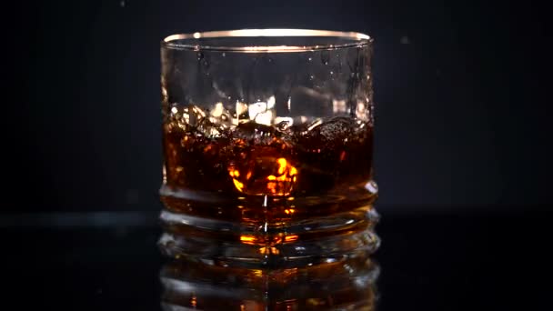 Um copo de whisky com cubo de gelo. Barman deixa cair cubos de gelo no copo com álcool. Uísque com gelo. Tiro deslizante. Escuro, rústico, fundo. — Vídeo de Stock