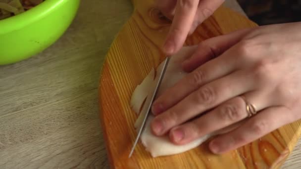 Куряче філе на обрізаній дошці. Жінка з ножем нарізає тонке куряче філе на дерев'яній дошці. Куряче м'ясо на столі . — стокове відео