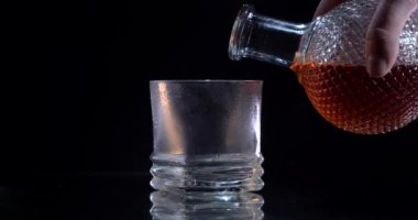 Mans siyah arka planda soğuk bardağa viski döküyor. Lüks içecek..