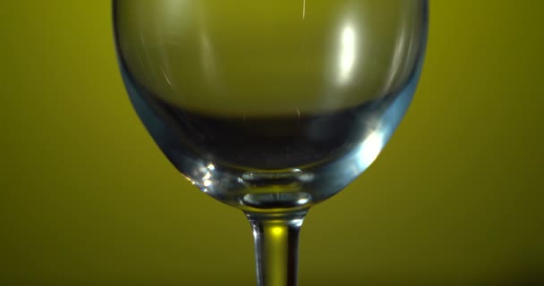 Egy közeli kép a borospohárról pirossal. Vörös bort öntök a serlegbe. A vörösbor gyönyörű hullámot alkot az üvegben. Gyönyörű sárga háttér — Stock videók