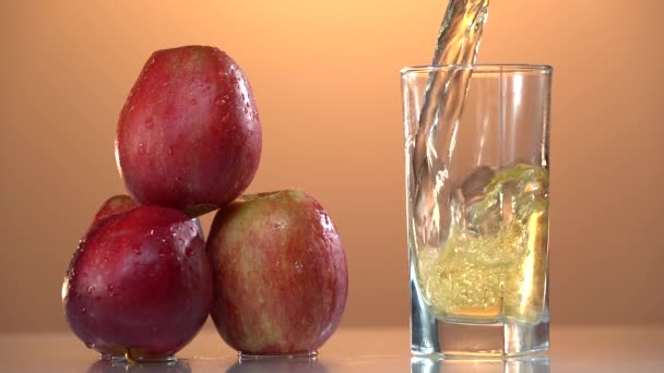 Taze elma suyunu bardağa, kırmızı elmaları da turuncu arka fona döküyor. Ağır çekim. Sağlıklı yemekler, vitaminler, meyveler. Yaz havası — Stok video