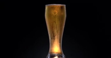 Siyah arka planda bir bardak siyah bira. Bardakta bira sallanıyor, kabarcıklar ve köpük yükseliyor. Bir bardak bira saat yönünde döner..