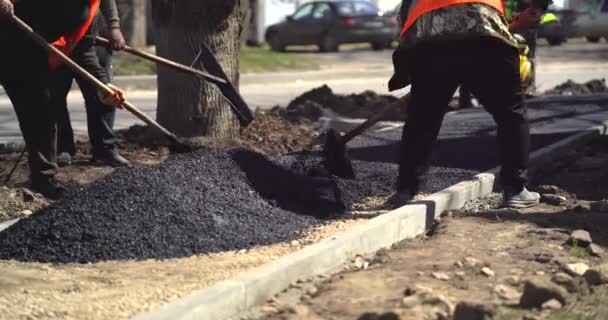 Weg reparatie. Werknemers leggen asfalt. Een klasser werkt op de achtergrond. Wegenwerkers verdelen asfaltmengsel. Wegenherstelling, nieuwe wegenbouw. — Stockvideo