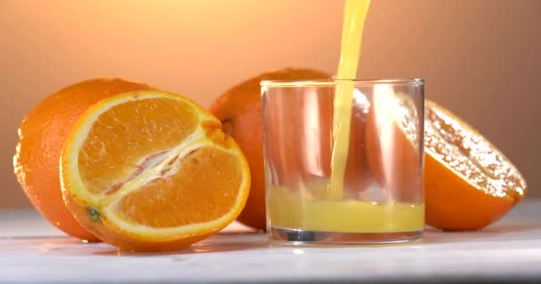 Bardakta ve portakalda sağlıklı taze portakal suyu. Kadın doluyor. Meyve suyu yavaş çekim görüntüsü yayar. 4K 'deki yakın çekim görüntüleri. Camın etrafında erkek portakalları. Renk arkaplanı — Stok video