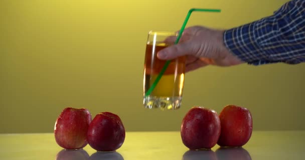 Mans mão colocar o copo com suco de maçã na mesa. Maçãs frescas sobre fundo amarelo — Vídeo de Stock