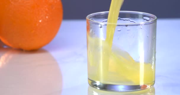 Häll apelsinjuice i glaset. Blå bakgrund. Färsk juice ligger på bordet. Sommarstämning — Stockvideo