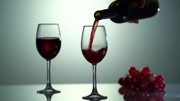 Víno. Nalévání červeného vína do skla z láhve na černém pozadí. Kamera se pohybuje kolem láhve a sklenice vína. Zpomalený záběr zblízka — Stock video