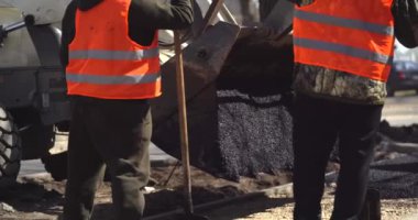 İki yol işçisi gün batımında bir kaldırıma sıcak asfalt döküyorlar. Yol yapımı makineler. Yol tamiri. Güzel güneş parlıyor.