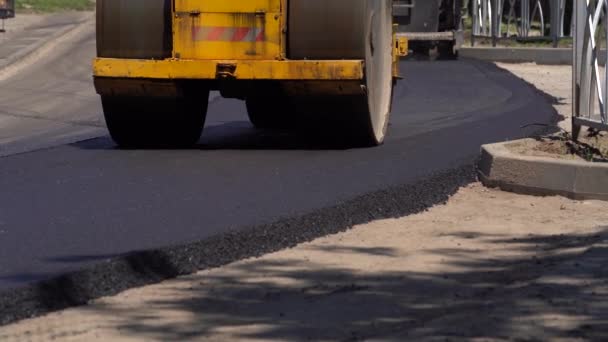 Kompaktor przejeżdża świeżo wylany asfalt i kompresuje go na drodze, aby naprawić dziurę. Zbliżenie rolki drogowej, która toczy się nowy gorący asfalt. Warstwa świeżo ułożonego asfaltu. Naprawa nawierzchni dróg. — Wideo stockowe