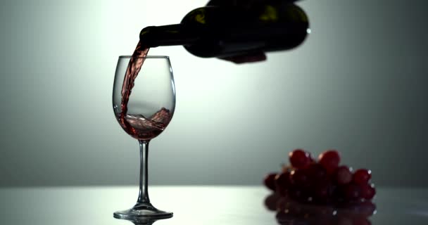El vino tinto forma una ola hermosa. Vino vierte en copa de vino sobre fondo blanco. Primer plano de tiro. Movimiento lento de verter vino tinto de la botella en la copa. — Vídeo de stock