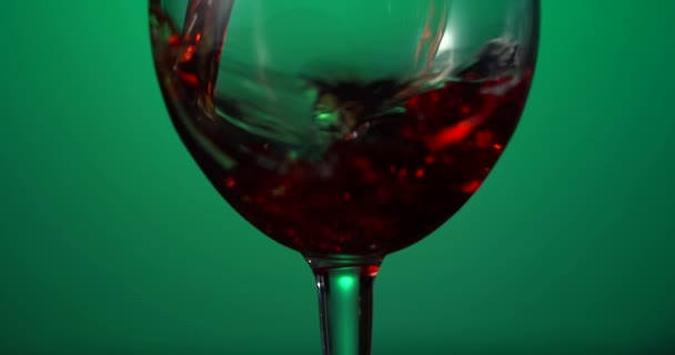 Le vin rouge forme une belle vague. Vin versé dans un verre de vin sur fond vert. Gros plan. — Video