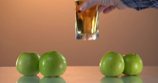 Mans hant poner el ingenio de cristal jugo de manzana fresca en la mesa. Haciendo jugo fresco. Captura detallada en cámara lenta de verter delicioso jugo de manzana en un vaso transparente sobre fondo blanco. De cerca. — Vídeos de Stock