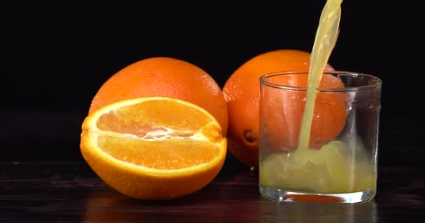 Den Orangensaft in das Glas auf schwarzem Hintergrund gießen. Frische Orangen liegen auf dem Tisch — Stockvideo