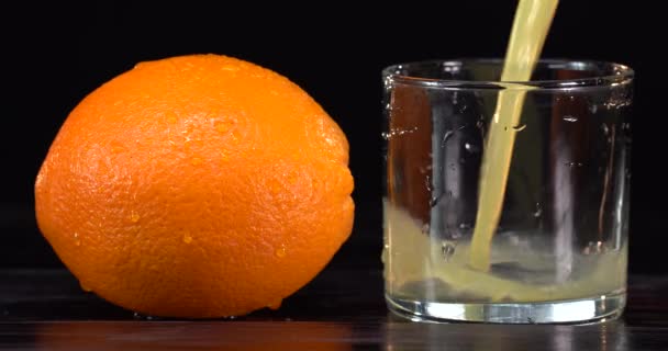 Verter jugo de naranja de una botella de vidrio sobre el fondo negro — Vídeo de stock