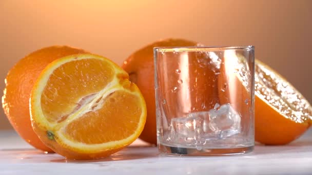 Das Eis für Orangensaft ins Glas geben. Frische Orangen liegen auf dem Tisch — Stockvideo