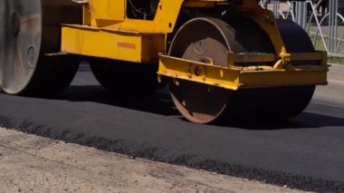 Batan güneşin ışınlarında yeni serpilmiş bir asfalt tabakası. Yol yüzeyi tamiri. Yeni bir yol inşaatı. Tekerlekler asfaltı düzleştirir ve sıkıştırır. Yol silindirleri. Güneş parlıyor.