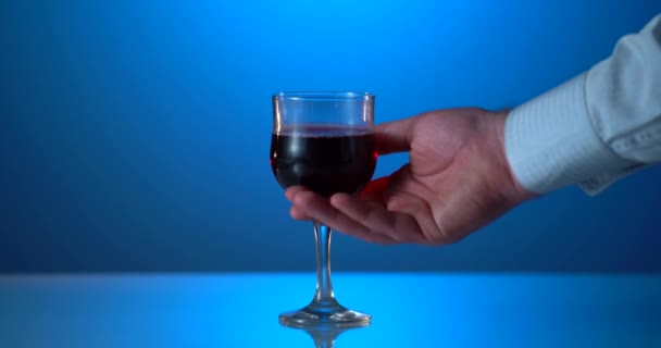 Mans kézzel veszi a pohár vörösbor a tükrözött asztal. Kék háttér — Stock videók