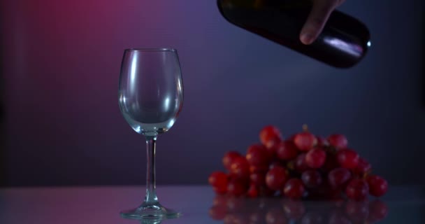 Rode wijn vormt een prachtige golf. Wijn gieten in wijnglas op dramatische achtergrond. Een close-up schot. Langzame beweging van het gieten van rode wijn uit fles in beker. — Stockvideo