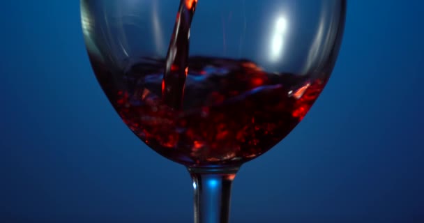 Verter vino tinto forma una hermosa ola. Vino vierte en copa de vino sobre fondo azul. Primer plano de tiro. Tecla baja — Vídeos de Stock