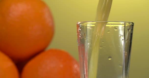 Vierte jugo de naranja en el vaso. fondo amarillo. Naranjas frescas están sobre la mesa — Vídeo de stock