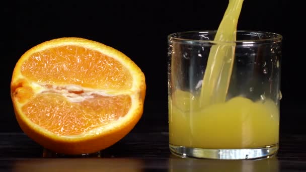 Γεμάτο φρούτα. Αργή κίνηση shot του ρίχνει χυμό πορτοκαλιού σε ένα διαφανές γυαλί σε μαύρο φόντο. Υγιεινό ποτό, βιταμίνες, φρούτα. Ποτήρι πλήρωσης με χυμό πορτοκαλιού close up 4K video — Αρχείο Βίντεο