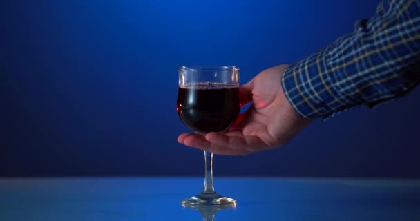 Glas av vackra åldrade rött vin mot blå bakgrund. Vinprovning och vinframställningskoncept. Kvinna hand håller och lätt skakar glas rött vin. Vinka rött vin i glas — Stockvideo