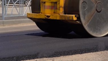 Batan güneşin ışınlarında yeni serpilmiş bir asfalt tabakası. Yol yüzeyi tamiri. Yeni bir yol inşaatı. Tekerlekler asfaltı düzleştirir ve sıkıştırır. Yol silindirleri. Güneş parlıyor.