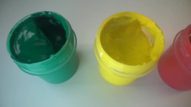 Beyaz yüzeyde yeşil, kırmızı ve sarı boya kutuları. Ressam allığı kırmızı renge batırır. Üst Manzara. Makro çekim