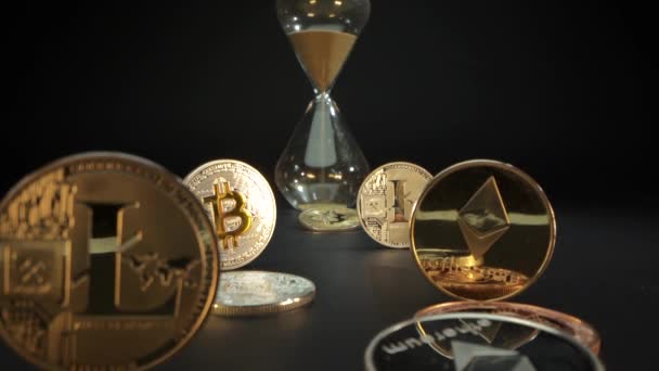 Viele Gold-Kryptomünzen auf der schwarzen Oberfläche Bitcoin, Etherium, Litecoin. Männliche Hand dreht die Sanduhr. Zeit ist Geld. Bitcoin ist der wichtigste digitale Wert — Stockvideo