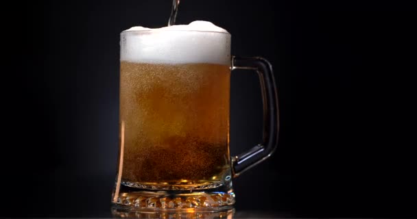 Alkohol. nalévat pivo z láhve do poslední kapky. Světlé pivo se sype do skla. Studené pivo ve sklenici s kapkami vody. Craft Beer tvořící pěnu zblízka. Čerstvost a pěna. Izolovaná černá — Stock video