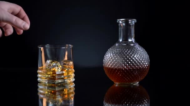 Man takes glass with alcohol. Pouring whiskey on vintage wooden table. Dark background. Bar — Stock Video