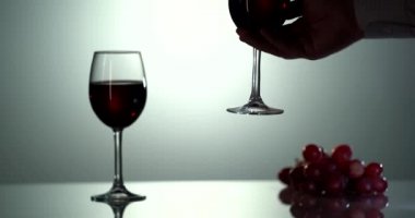 Siluet adam eli yansıyan yüzeyi olan kırmızı bir şarap ile bardağı alır.