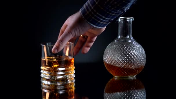 El hombre toma alcohol después de una semana larga y difícil. Whisky dorado en el vaso de la botella. Con hielo cubos. Reflexiona sobre la mesa. Concepto de bar — Vídeo de stock