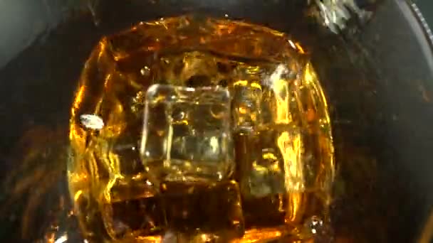 El hermoso líquido dorado está corriendo a través de los cubos de hielo en una copa de cóctel. Primer plano dramático y cámara lenta extrema. Obras para sidra, cerveza, prosecco, vino rosa, zumo, ron, licor, whisky. — Vídeo de stock