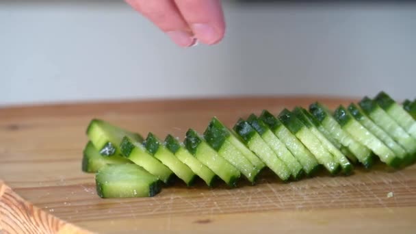 Womens hands puts a salt into the cucumber on a wooden board, close-up. — Stock Video